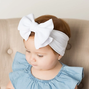 Close-up of white waffle knit baby headband with a large decorative bow on an infant
