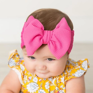Detailed close-up of a baby girl wearing a pink textured fabric bow headband on a white backdrop