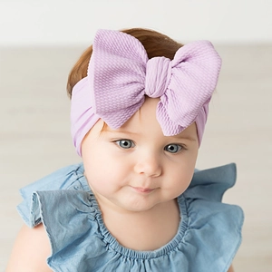Detailed close-up of a lilac ribbed fabric infant headband with a large bow on a baby
