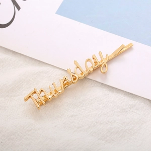 Close-up of golden alloy hair clip featuring Thursday letter design on white fabric