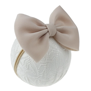 Détail d'un bandeau pour bébé avec un grand nœud rose poudré sur support en dentelle