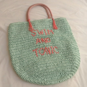 Detail of mint green woven tote bag with pink Swim and Tonic embroidery and tassel