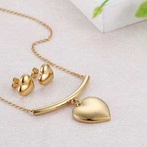 Elegant gold heart pendant necklace and matching stud earring set on marble background