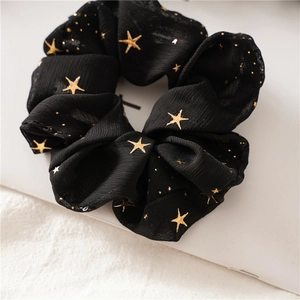 Close-up of black chiffon scrunchie featuring gold foil star patterns and soft pleats