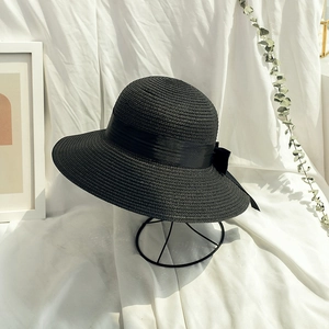 Detailed close-up of a black straw sun hat featuring an elegant ribbon bow on a stand