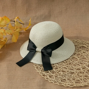 Detail of cream straw sun hat with black satin ribbon bow on a textured rustic background