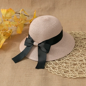 Detail of pink straw sun hat with woven texture and a large black ribbon bow on linen