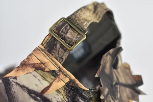 Macro detail of the bronze metal adjustment buckle on a bionic camo leaf hunting cap