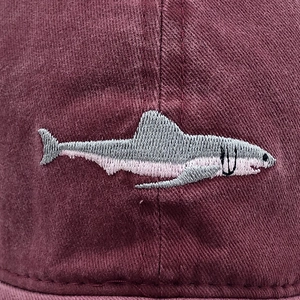 Detailed close-up of shark embroidery on a burgundy cotton washed baseball cap