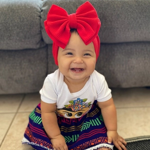 Close-up of baby girl wearing oversized red bow headband and colorful tribal pattern skirt