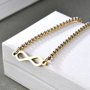 Dettaglio del bracciale dorato con simbolo dell'infinito su un portagioie in pelle bianca