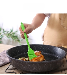 Green silicone pastry brush applying oil to meat in a kitchen cooking scene