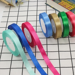 Glossy satin ribbon rolls in multiple colors for gift wrapping on checkered fabric