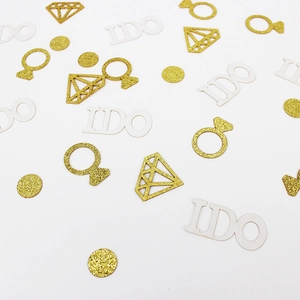 Macro detail of gold glitter diamond rings and white I DO wedding confetti decorations
