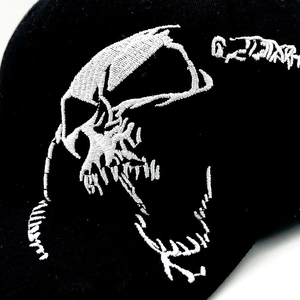 Close-up of intricate white skull embroidery on black cotton fabric of a baseball cap
