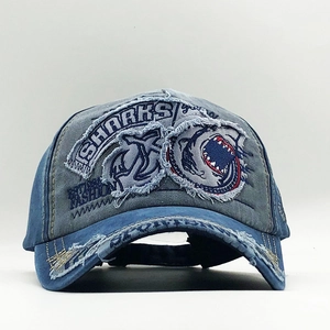 Close-up of blue distressed denim baseball cap with shark patches and frayed edges