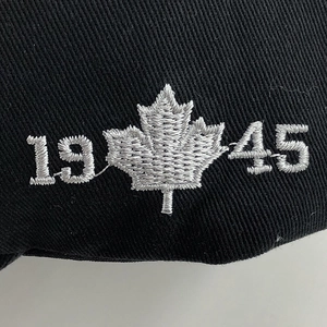 Macro detail of silver maple leaf and 1945 embroidery on a black cotton baseball cap