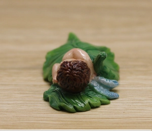 Macro detail of miniature sleeping baby figurine on green leaf with resin wings