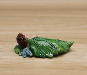 Macro detail of sleeping baby fairy figurine in green leaf with blue wings for garden