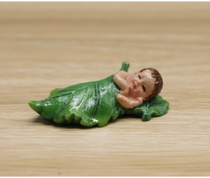 Detailed macro view of sleeping baby resin figurine nestled in a green leaf ornament