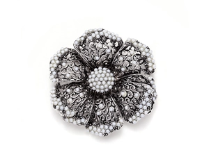 Macro detail of vintage floral brooch featuring silver filigree and pearl accents