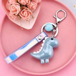 Close-up of blue dinosaur keychain with iridescent wrist strap on a pink display tray