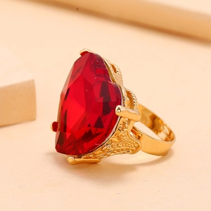 Elegant gold ring featuring a large heart-shaped red gemstone with intricate cutwork