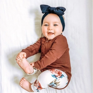 Close-up of a baby wearing a ribbed brown romper with a large floral bow headband
