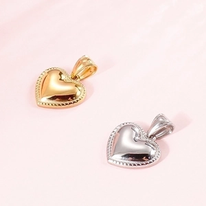 Polished gold and silver heart pendants with beaded edges on a soft pink background