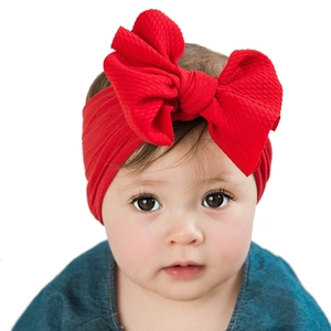 Infant wearing a red knotted fabric headband with a large bow on a white background