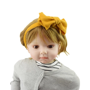 Close-up of a lifelike baby doll wearing a yellow bow headband and grey knit cardigan