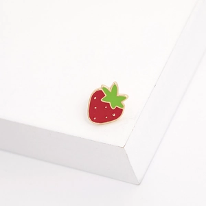 Detailed view of red strawberry enamel brooch with gold accents on white surface