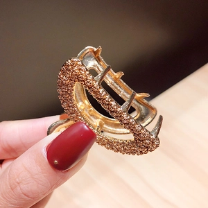 Golden geometric claw clip with 3D rose relief texture shown in hand for size context