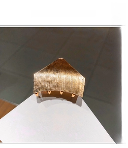Detail of gold metal hair claw with vertical striped texture and geometric fold design