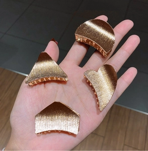Close-up of golden geometric metal hair clips with brushed finish in hand