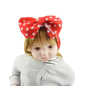 Detail of red polka dot bow headband on baby doll with soft fabric texture
