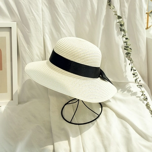 Detail of a woven straw hat with a wide black ribbon bow on a minimal display stand