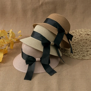 Detail of woven straw hats featuring elegant black silk ribbon bows for beach sun protection