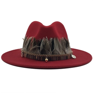 Detail of red fedora hat featuring ethnic ribbon, natural feathers and metal charms