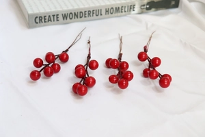 Detailed view of four red artificial berry stems on white fabric for DIY home decor