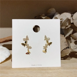 Close-up of golden butterfly earrings with sparkling white zircons on a minimal card
