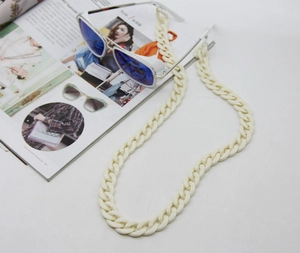 Close-up of thick cream acrylic eyewear chain with blue reflective sunglasses on a magazine