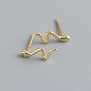 Close-up of gold snake earrings featuring sparkling zirconia studs on a grey surface