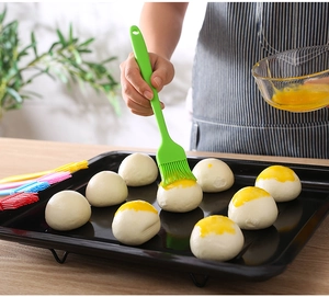 Detail of a green silicone basting brush applying egg wash onto raw dough for baking