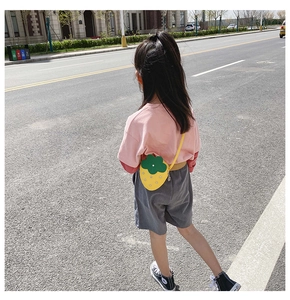 Kid's yellow strawberry crossbody bag with green leaf detail worn on shoulder