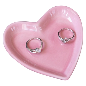 Pink heart-shaped ceramic jewelry tray with silver rings on a clean white background