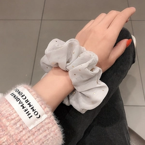 Detail of a white chiffon scrunchie with gold star pattern worn on wrist for styling