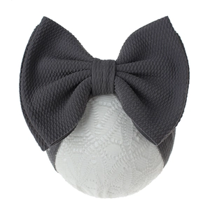 Detail of baby headband featuring large dark grey waffle bow and white lace texture base