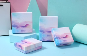 Multiple jewelry gift boxes with pink-purple cloud art and matching blue paper bag