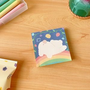 Detailed close-up of a cute cartoon sheep on a rainbow memo pad with floral accents